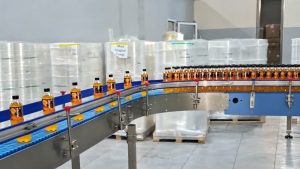 ПЭТ-бутылки с оранжевым напитком движутся по изогнутому конвейеру на линии розлива.